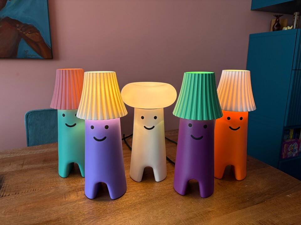 Vijf gezichtjeslampen aan op een houten tafel: groen, lila, wit met paddenstoelhoed, paars en oranje