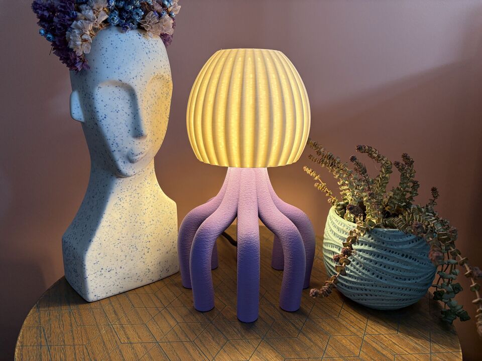 Paarse octopuslamp met witte bolkap aan, naast een vaas in de vorm van een gezicht
